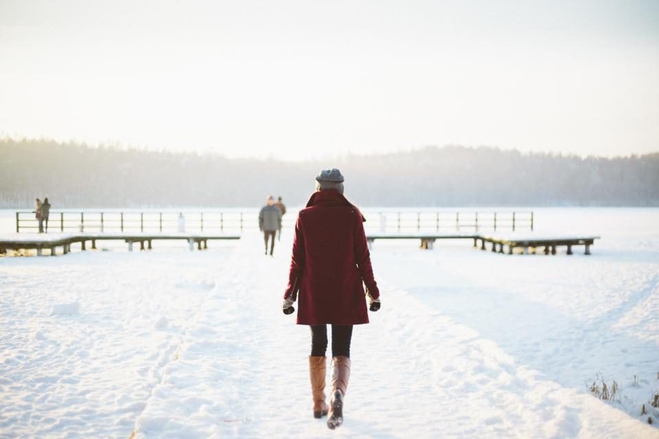 Kobieta idąca zimą zaśnieżonym pomostem nad jeziorem